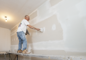 Andy Delege applying mud to drywall while on scaffolding in housing addition project in Victoria BC